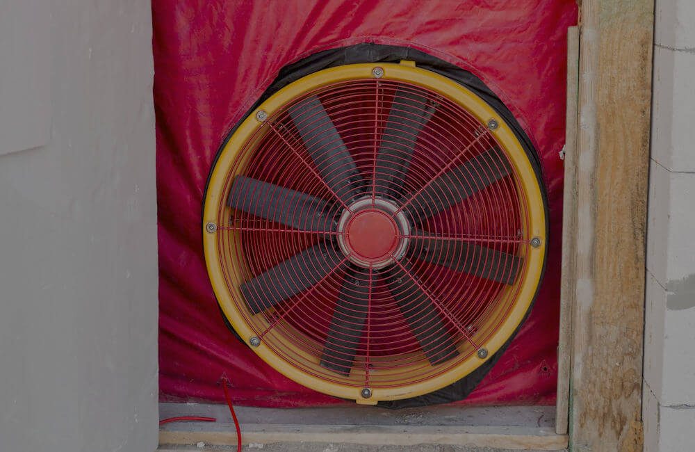 A Retrotec blower door fan set into a doorway aperture, sealed with a red sheet