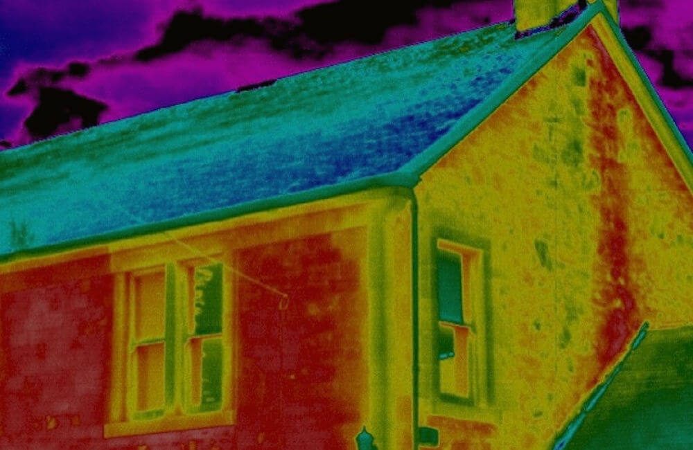 Thermal image of a gable wall: a cool roof surface, warmer wall faces in yellow and red, and colder window openings